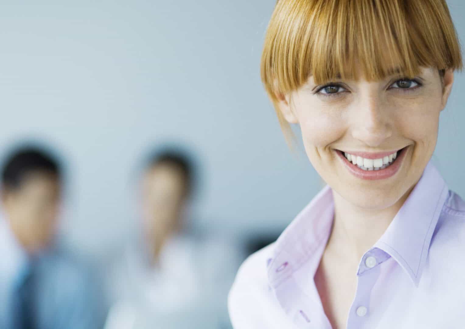 Smiling businesswoman with colleagues blurred.