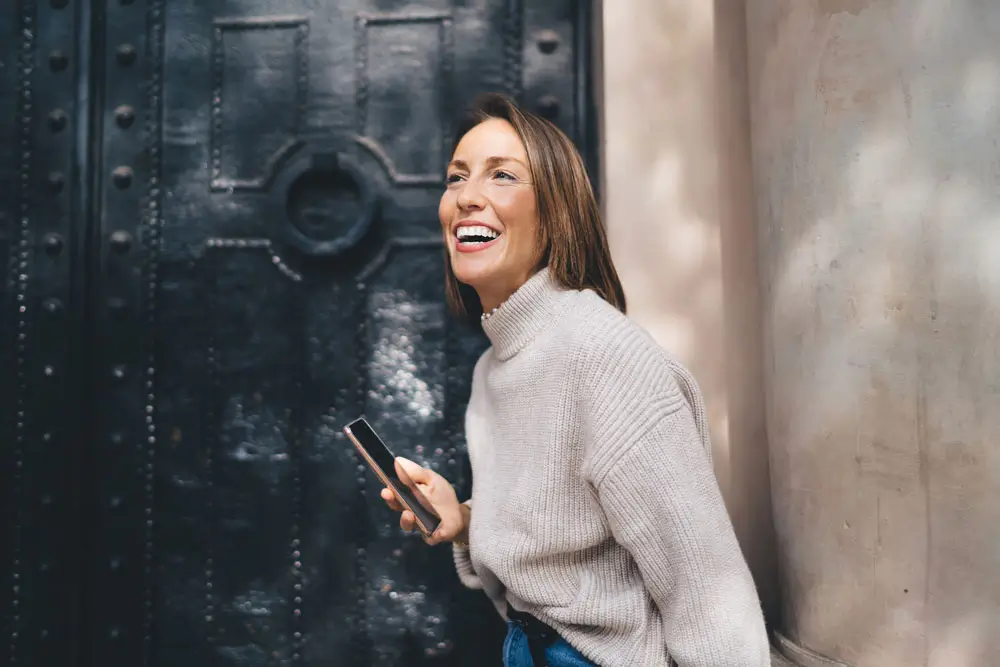Test Dental Implants 46 Happy woman using phone outdoors.