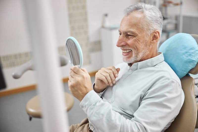 Test Dentures Illinois 1 Senior man admires his new smile.