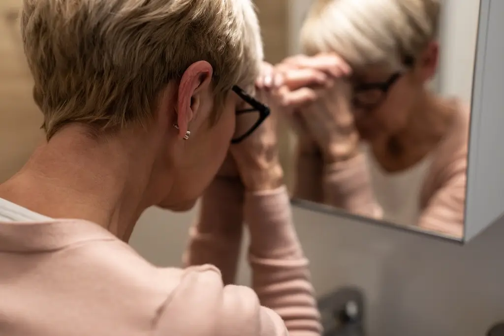 Dental Implants Lisle 1 Woman looking stressed in mirror.