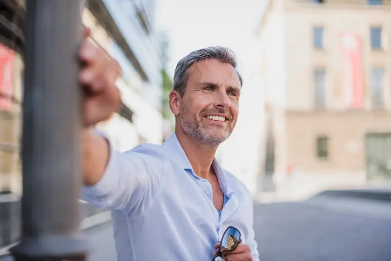 Dental Implants Lisle 47 Smiling man in city, holding sunglasses.